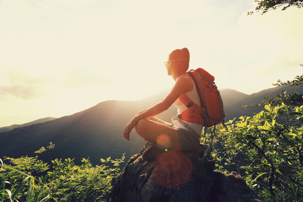 Woman backpacker sit on sunrise mountain peak cliff rock enjoy the view
