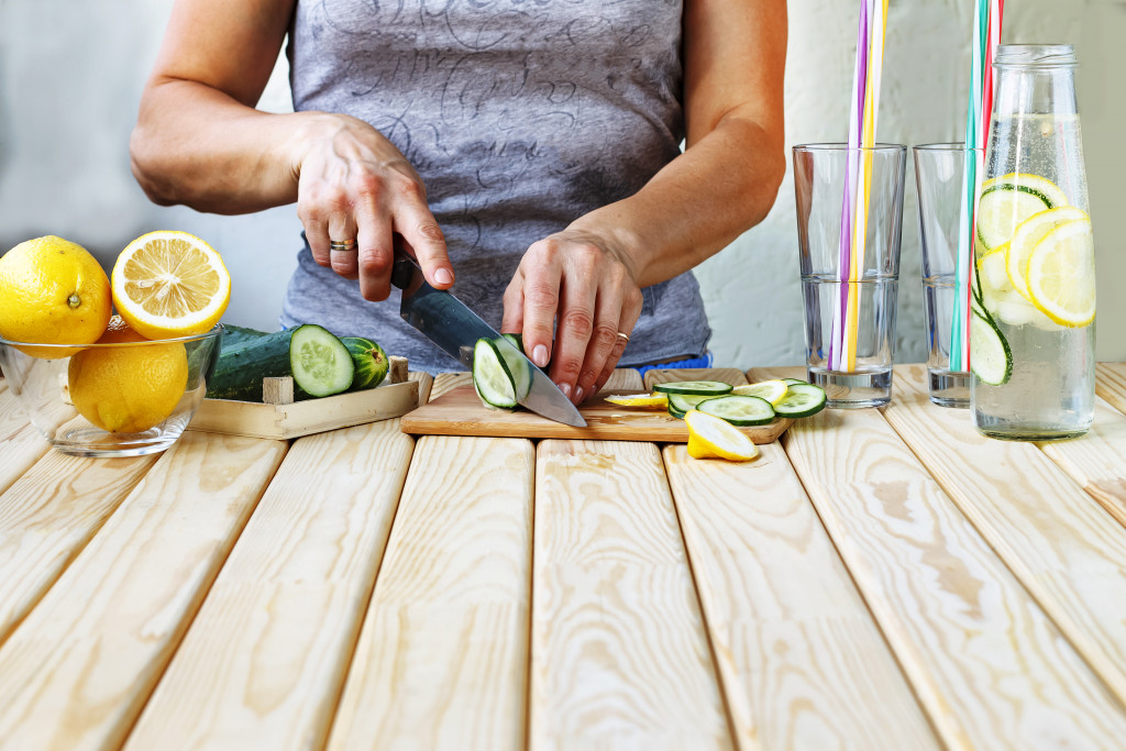 Woman cutting fruits and vegetables on a cutting board on a table in the kitchen.