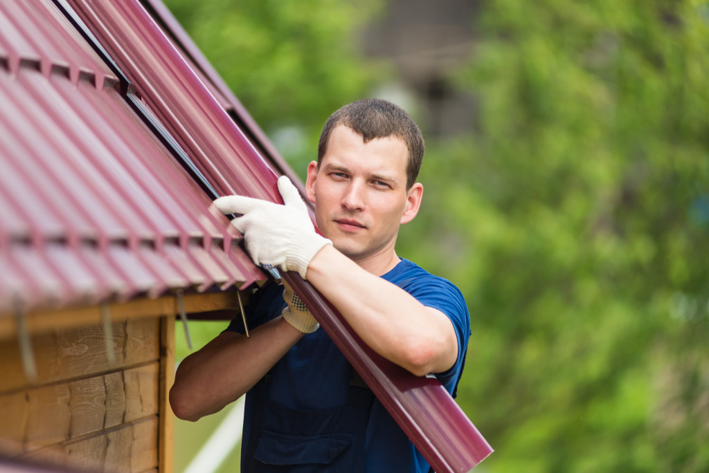 A homeowner wearing gloves lifts up a rolled-up sheet of metal roofing