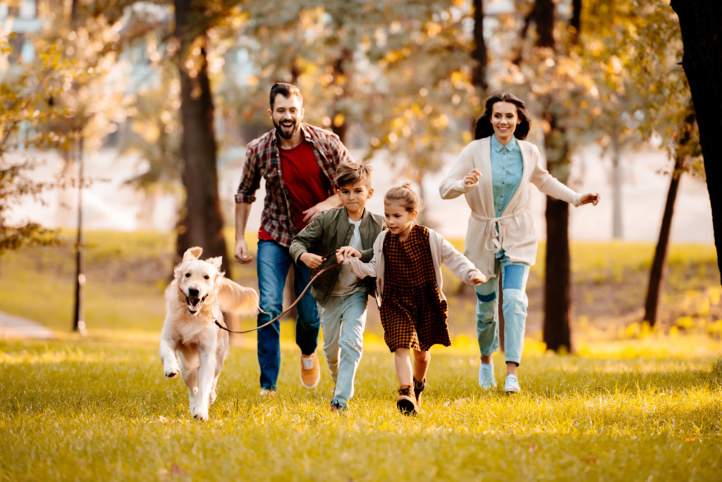 happy family running with dog on grassfield setting