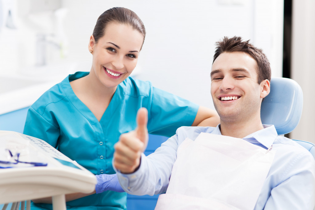 a male patient on a dentist chair with thumbs up beside a dentist